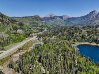 Experience the ultimate mountain lifestyle with this stunning aerial view of a property nestled amidst lush green forests and overlooking a serene blue lake.
