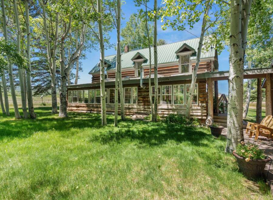 Nestled amongst mature aspen trees, this charming log home offers a serene retreat with its rustic architecture and picturesque setting.
