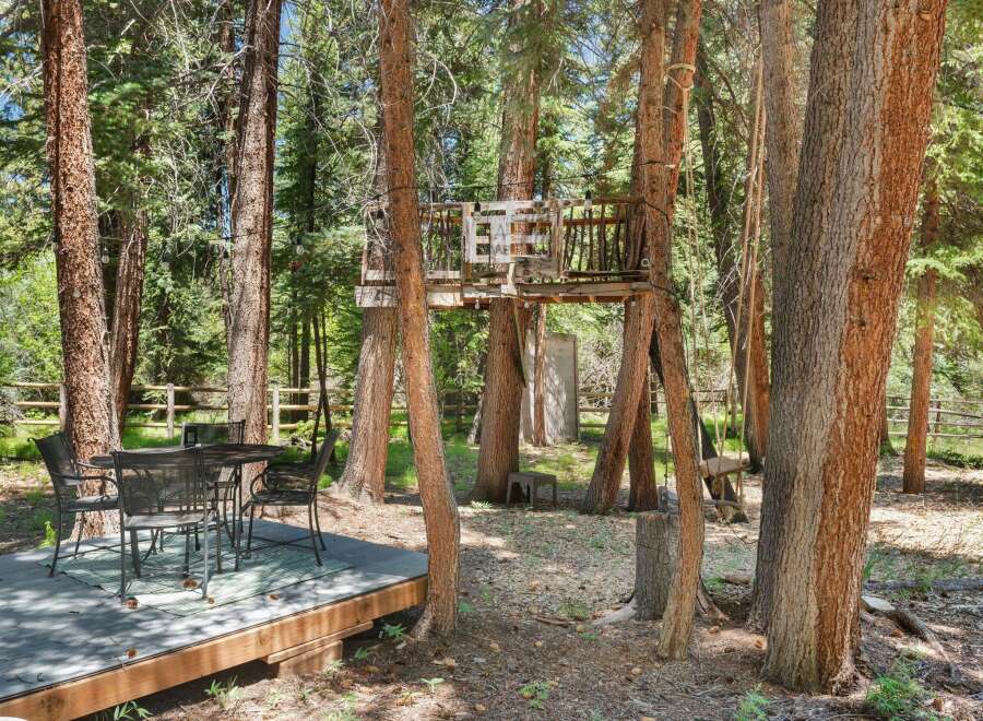 Enjoy the outdoors with this charming backyard setup, featuring a rustic treehouse and a dining area perfect for al fresco meals.