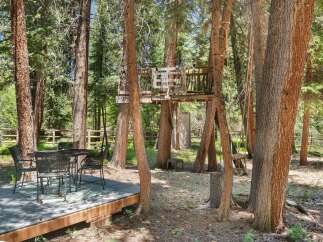 Enjoy the outdoors with this charming backyard setup, featuring a rustic treehouse and a dining area perfect for al fresco meals.