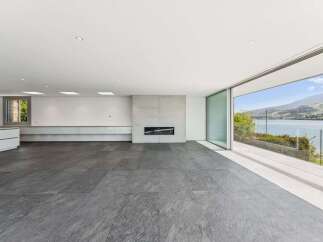 Experience modern living with this stunning open-concept living space, featuring a sleek concrete fireplace and expansive sliding glass doors that open to breathtaking lake and mountain views.
