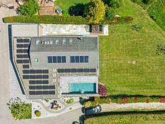 Experience modern living with this stunning aerial view showcasing a property with an abundance of solar panels, a sleek swimming pool, and a beautifully landscaped garden.