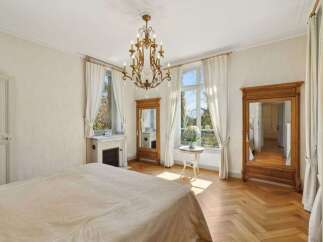 Experience elegant living in this charming bedroom featuring a classic fireplace and a grand chandelier.