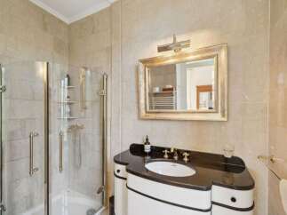 Experience luxury in this elegant bathroom featuring a spacious glass-enclosed shower with polished brass fixtures and a sleek vanity with a dark granite countertop.