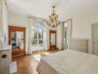 Experience elegant living in this beautifully appointed bedroom, featuring a grand chandelier and large windows that flood the space with natural light.