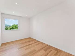Experience modern living in this bright and airy room featuring a large window with scenic views of lush greenery and distant mountains.