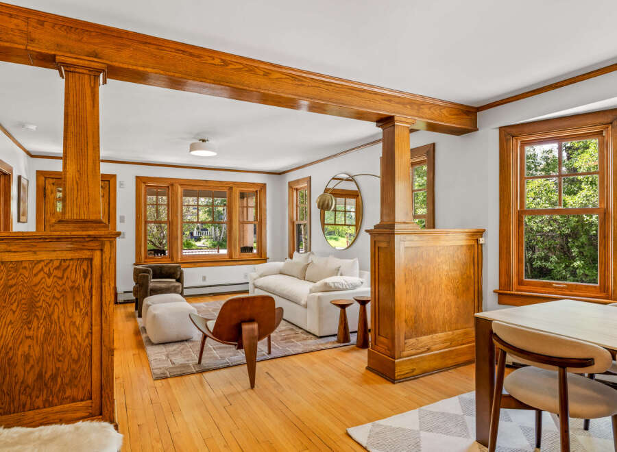 Step into this beautifully appointed living and dining area, featuring rich hardwood floors and stunning natural light pouring in through large wooden-framed windows.