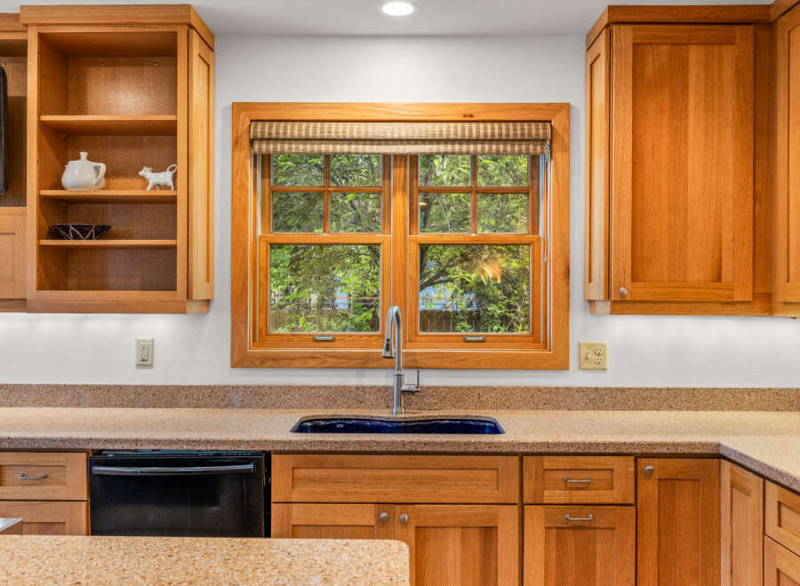 This kitchen features beautiful natural wood cabinetry and a large window overlooking lush greenery, bringing the outdoors in.