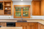 This kitchen features beautiful natural wood cabinetry and a large window overlooking lush greenery, bringing the outdoors in.