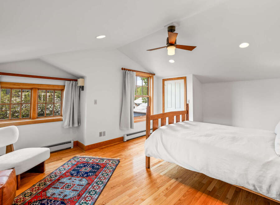This charming bedroom features a cozy wooden bed dressed in crisp white linens, complemented by a vibrant oriental rug on the gleaming hardwood floor.