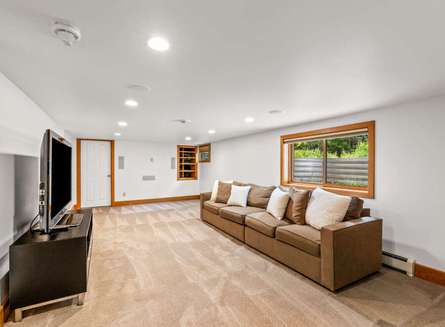 This spacious basement living area features a comfortable brown sectional sofa adorned with plush pillows, perfect for relaxing.
