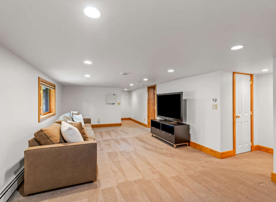 This spacious basement living area features a comfortable brown sofa with accent pillows, perfect for relaxing.