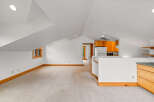 Discover this charming attic space featuring a cozy living area with plush carpeting and a convenient kitchenette equipped with wooden cabinetry and a refrigerator.