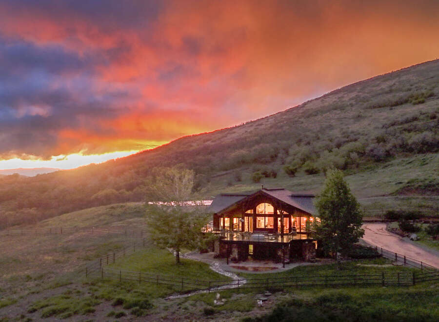 Experience breathtaking sunset views from this stunning mountain lodge, featuring a spacious deck perfect for entertaining and a cozy interior illuminated by warm lights.