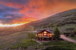 Experience breathtaking sunset views from this stunning mountain lodge, featuring a spacious deck perfect for entertaining and a cozy interior illuminated by warm lights.