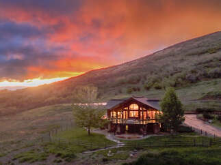 Experience breathtaking sunset views from this stunning mountain lodge, featuring a spacious deck perfect for entertaining and a cozy interior illuminated by warm lights.