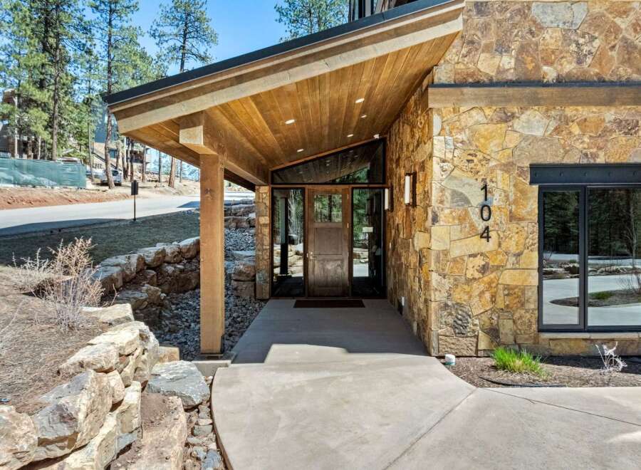 Discover modern mountain living with this stunning home featuring a striking stone facade and a dramatic angled wood-paneled entryway.