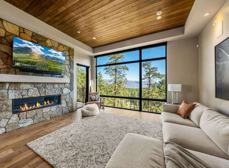 Experience breathtaking mountain views from this stunning living room, featuring a modern gas fireplace set against a natural stone accent wall.