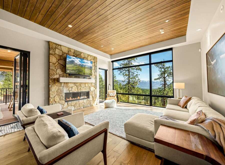 Experience breathtaking mountain views from this stunning living room, featuring a modern stone fireplace and a large, wall-to-wall window.