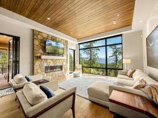 Experience breathtaking mountain views from this stunning living room, featuring a modern stone fireplace and a large, wall-to-wall window.
