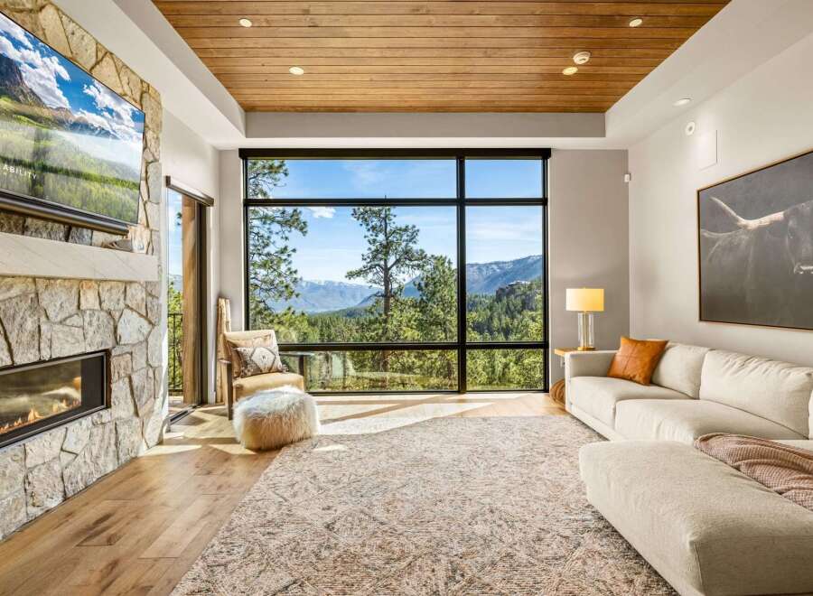 Experience breathtaking mountain views from this stunning living room, featuring a modern stone fireplace and a large, picturesque window.