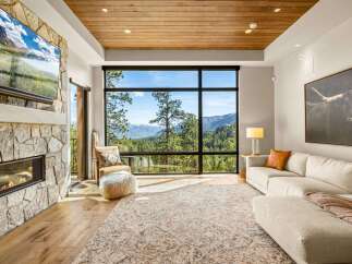 Experience breathtaking mountain views from this stunning living room, featuring a modern stone fireplace and a large, picturesque window.