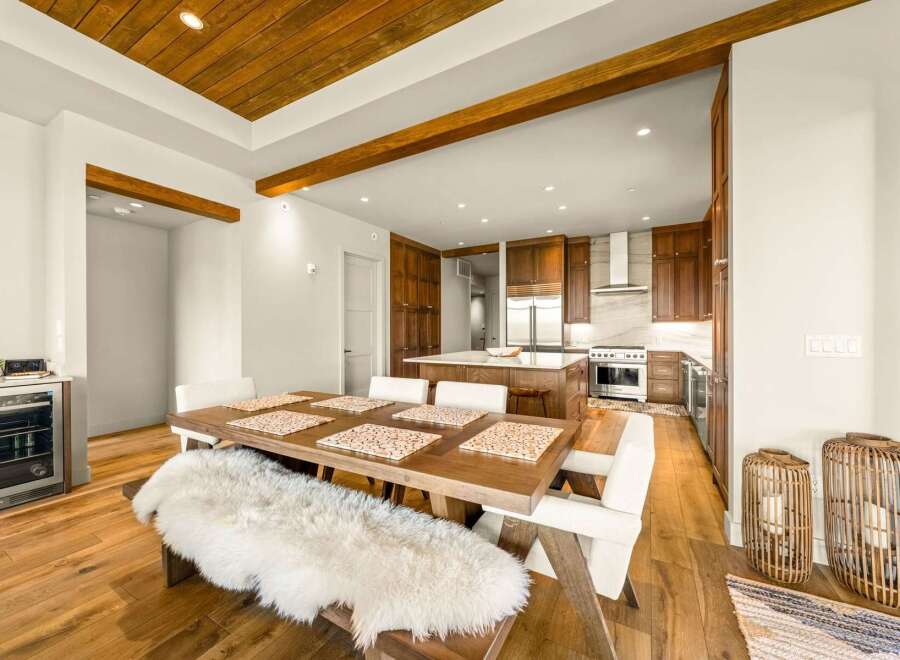 Experience modern luxury in this open-concept living space, featuring a stunning wood-paneled ceiling with exposed beams and a sleek, gourmet kitchen.