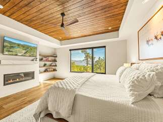 Experience luxury mountain living in this stunning bedroom featuring a modern gas fireplace and a wall-mounted TV for ultimate relaxation.