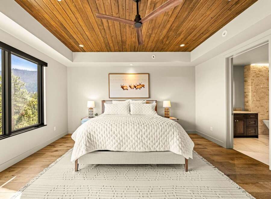 Experience luxury mountain living in this stunning bedroom featuring a warm wood-paneled ceiling and a large window with breathtaking views.