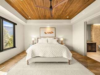 Experience luxury mountain living in this stunning bedroom featuring a warm wood-paneled ceiling and a large window with breathtaking views.