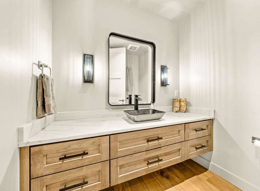 This modern bathroom features a sleek vanity with natural wood drawers and a white marble countertop.