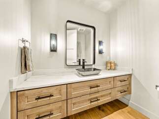 This modern bathroom features a sleek vanity with natural wood drawers and a white marble countertop.