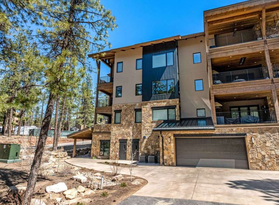 Experience luxury mountain living in this stunning multi-level residence, featuring a modern facade with stone accents and expansive balconies perfect for enjoying the surrounding pine forest.