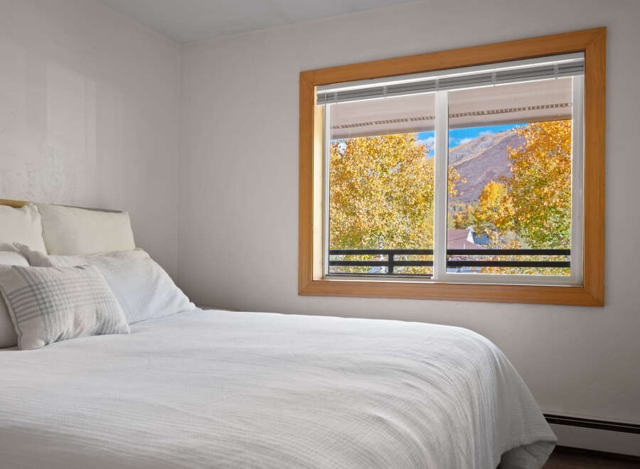Experience breathtaking autumn views from this cozy bedroom, featuring a comfortable bed and a large window showcasing vibrant fall foliage and majestic mountains.
