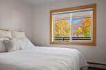 Experience breathtaking autumn views from this cozy bedroom, featuring a comfortable bed and a large window showcasing vibrant fall foliage and majestic mountains.