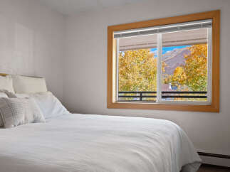 Experience breathtaking autumn views from this cozy bedroom, featuring a comfortable bed and a large window showcasing vibrant fall foliage and majestic mountains.