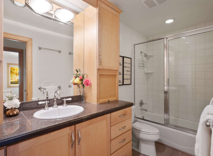 This bright and airy bathroom features a spacious vanity with ample storage and a granite countertop, complemented by a large mirror and elegant light fixtures.