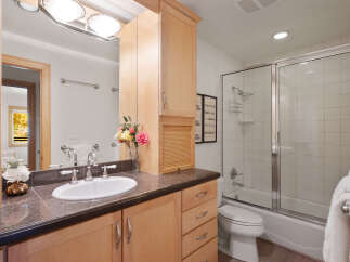 This bright and airy bathroom features a spacious vanity with ample storage and a granite countertop, complemented by a large mirror and elegant light fixtures.
