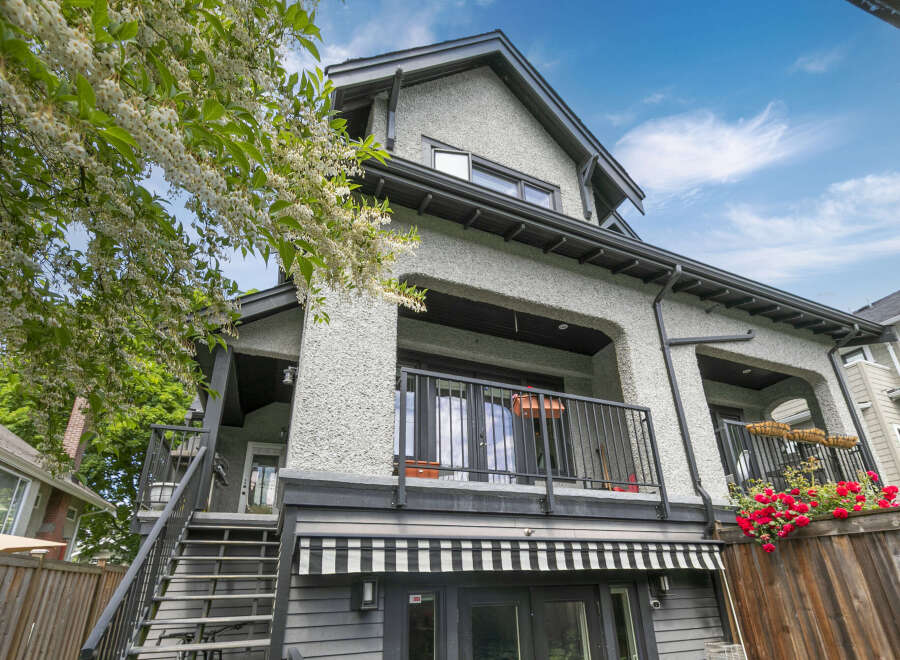 Charming home featuring a stucco exterior and a dark-trimmed roofline, complemented by lush greenery and vibrant red roses.