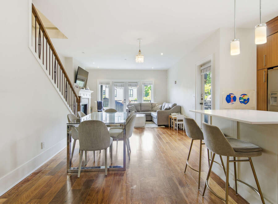 Experience modern living in this open-concept space featuring a sleek dining area with a glass-top table and upholstered chairs, adjacent to a stylish kitchen island with bar stools.