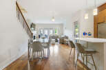 Experience modern living in this open-concept space featuring a sleek dining area with a glass-top table and upholstered chairs, adjacent to a stylish kitchen island with bar stools.
