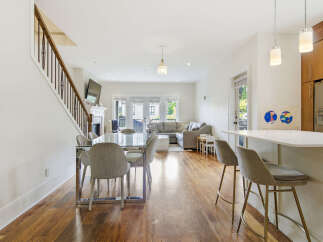 Experience modern living in this open-concept space featuring a sleek dining area with a glass-top table and upholstered chairs, adjacent to a stylish kitchen island with bar stools.
