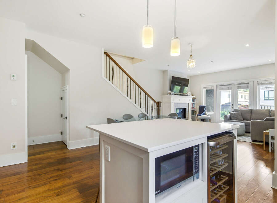 This modern open-concept living space features a sleek white kitchen island with integrated microwave and wine cooler, perfect for entertaining.