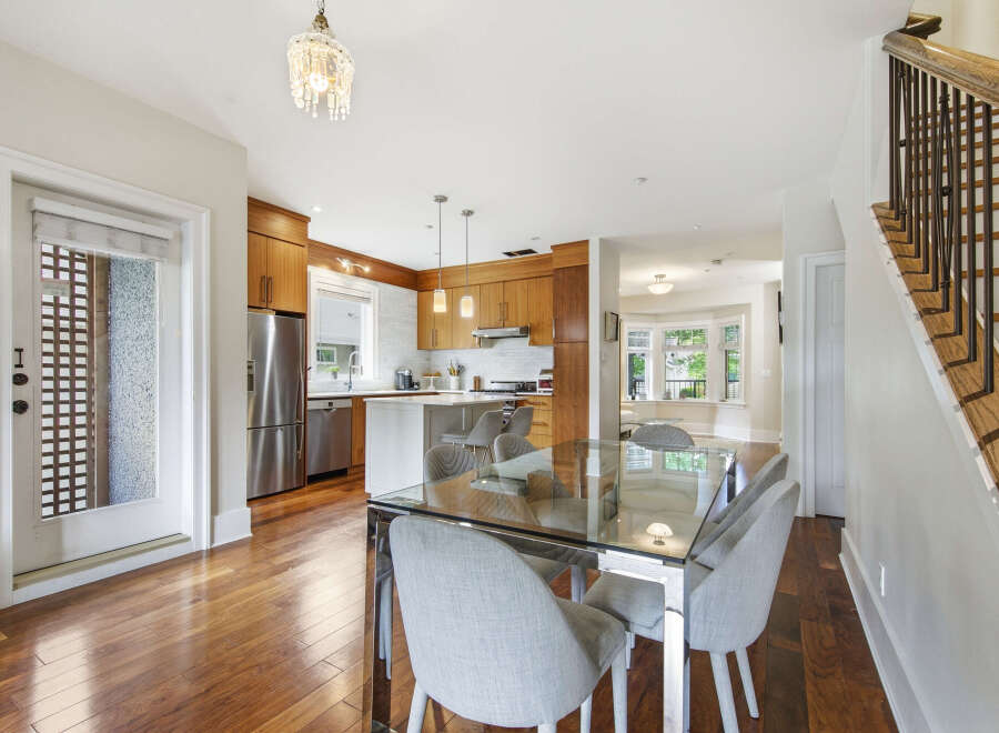 This spacious open-concept dining and kitchen area features a sleek glass-top dining table with comfortable upholstered chairs, perfect for family gatherings.