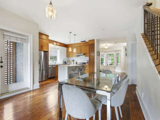 This spacious open-concept dining and kitchen area features a sleek glass-top dining table with comfortable upholstered chairs, perfect for family gatherings.