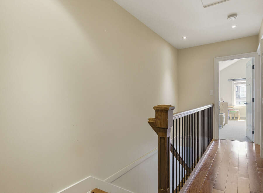 This hallway features a beautiful wooden staircase railing with dark spindles, leading to a bright room with natural light.