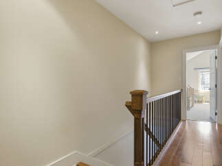 This hallway features a beautiful wooden staircase railing with dark spindles, leading to a bright room with natural light.