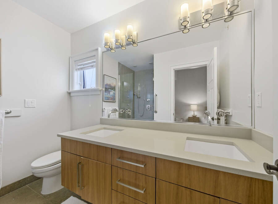 This modern bathroom features a sleek double vanity with a light-colored countertop and warm wood cabinetry, complemented by dual sinks and chrome fixtures.