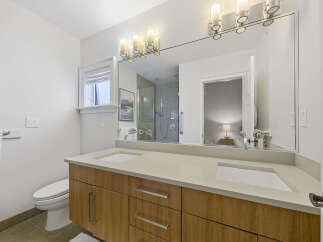 This modern bathroom features a sleek double vanity with a light-colored countertop and warm wood cabinetry, complemented by dual sinks and chrome fixtures.