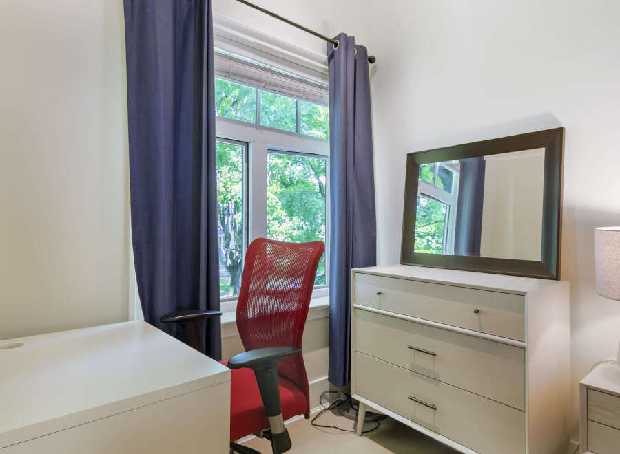 This bright and airy room features a comfortable red office chair positioned by a large window, offering a pleasant view of lush greenery.